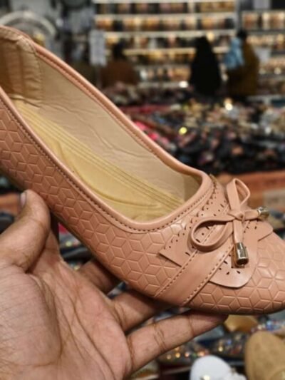 Peach colored ballet flat with bow detail held in hand, displayed in a jain chappal store located in delhi shahdara.