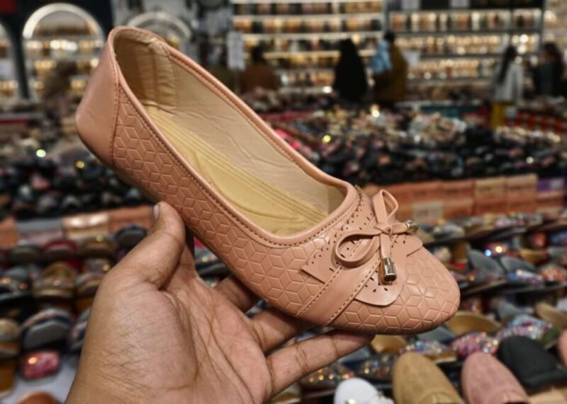 Peach colored ballet flat with bow detail held in hand, displayed in a jain chappal store located in delhi shahdara.