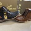 Two stylish Tiger Hill leather boots, one in black with brown accents and one in rustic brown, featuring lace-up and zipper designs, displayed on a tile floor at jain chappal store shahdara with branded packaging in the background.