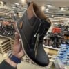 Two stylish Tiger Hill leather boots, one in black with brown accents and one in rustic brown, featuring lace-up and zipper designs, displayed on a tile floor at jain chappal store shahdara with branded packaging in the background.