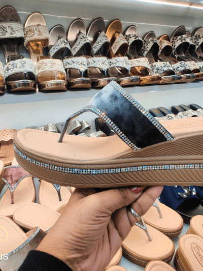 A stylish women’s platform sandal with a glossy black strap, cushioned footbed, and rhinestone-embellished sole, displayed in a footwear store.