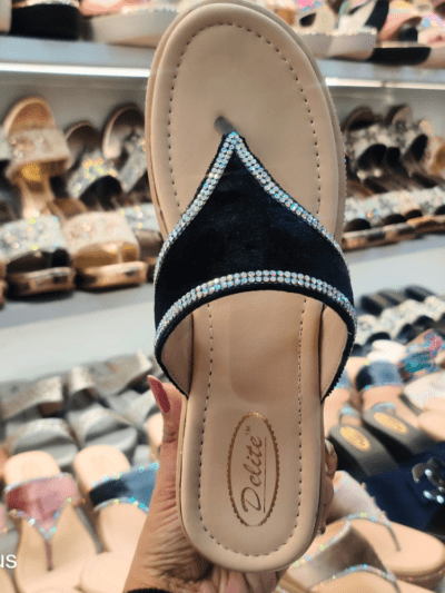 A stylish women’s platform sandal with a glossy black strap, cushioned footbed, and rhinestone-embellished sole, displayed in a footwear store.